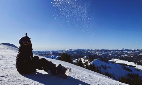 A snowboarder with an action camera on their head sits on the groomer.
