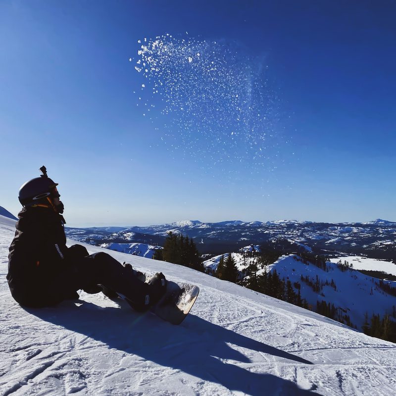 A snowboarder with an action camera on their head sits on the groomer.