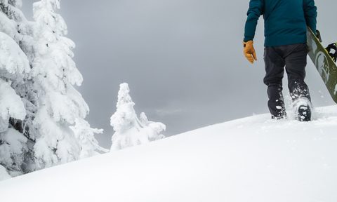 A man walks up a mountain in deep snow with a snowboard.