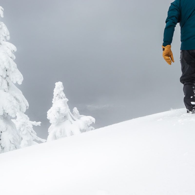 A man walks up a mountain in deep snow with a snowboard.