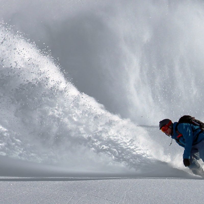 A man snowboarding with a rip of powder behind him.