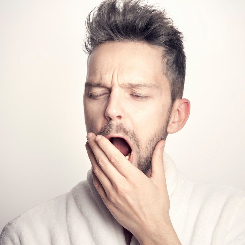 Man with eyes closed and yawning with hand near is mouth