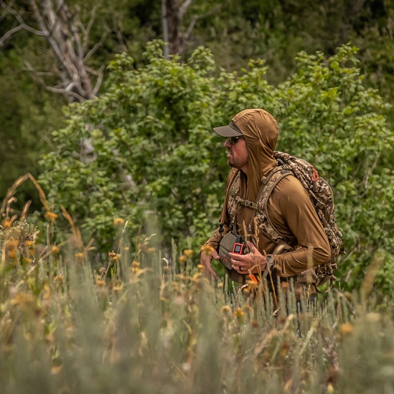 Man hiking through high grass in a Sitka Gear tan hoodie.
