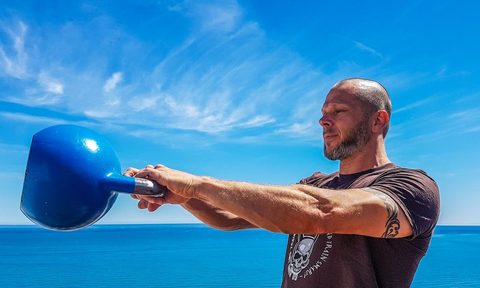 A man swinging a kettlebell by a blue sky