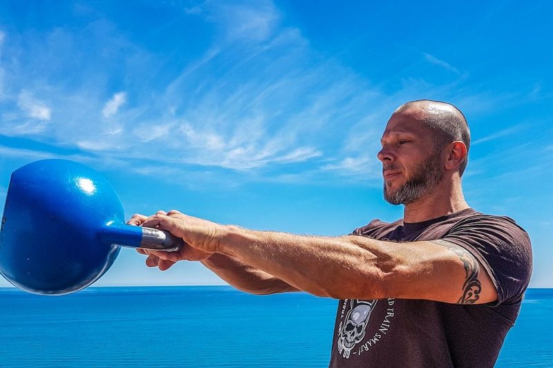A man swinging a kettlebell by a blue sky