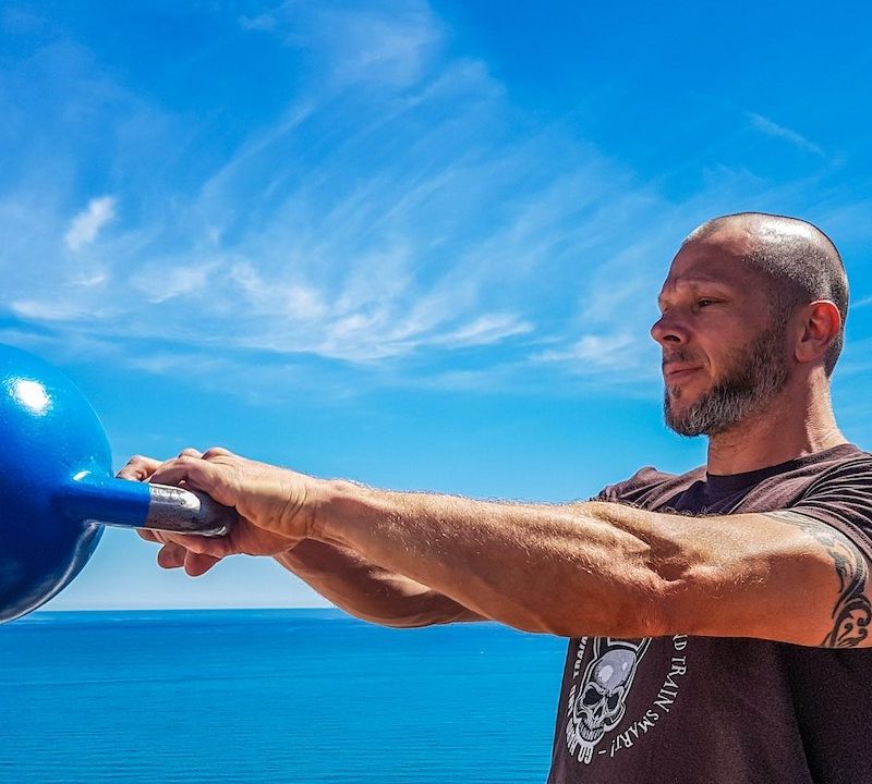 A man swinging a kettlebell by a blue sky