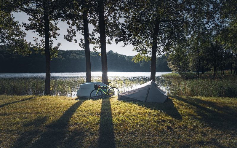 Bike and bikepacking tent setup near a heavily wooded pond.