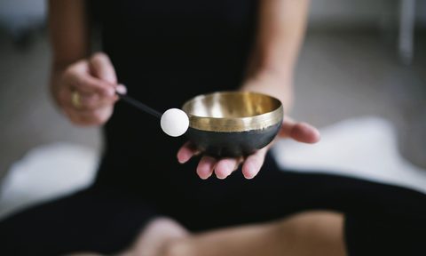 Person sitting cross legged on the ground holding a sound bowl.