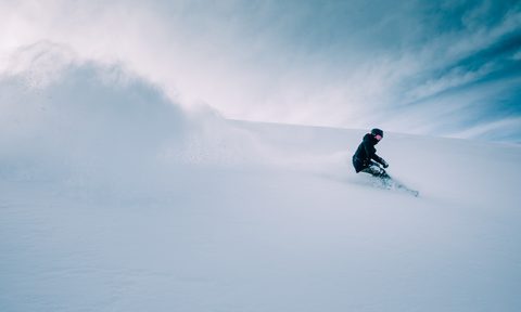 A person snowboarding in deep powder with clear skies behind them.