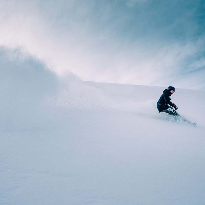 A person snowboarding in deep powder with clear skies behind them.