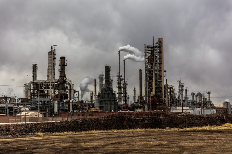Industrial plant spewing thick smoke under a dark, cloudy sky.