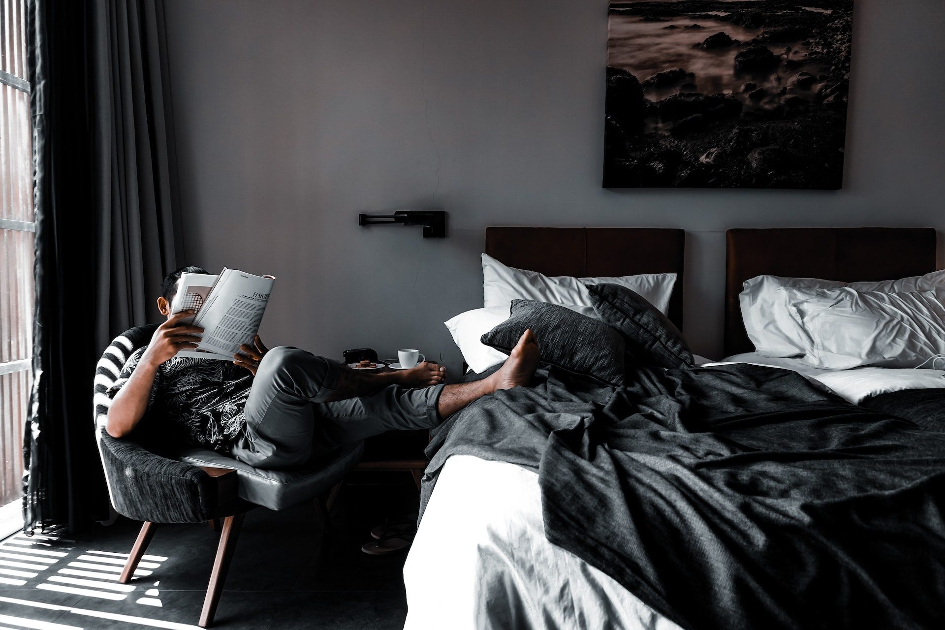 Man relaxing with a leg propped up on a hotel bed, reading