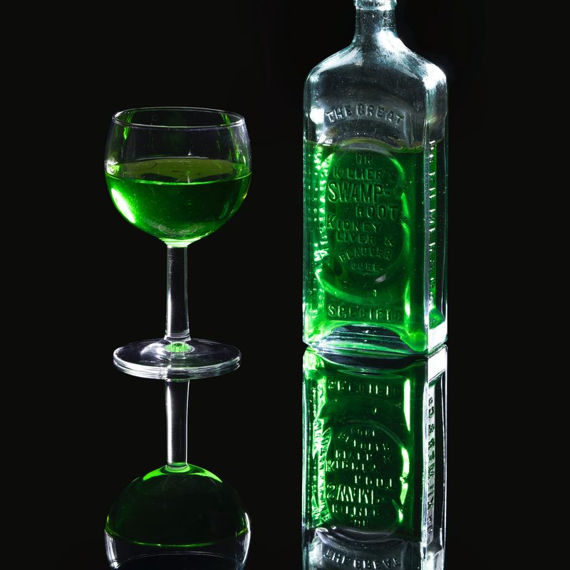 Absinthe in glass next to a bottle with a black background