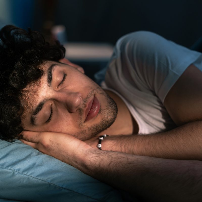 Handsome young man sleeping on pillow in dark room at night, resting at night time. Healthy sleep concept