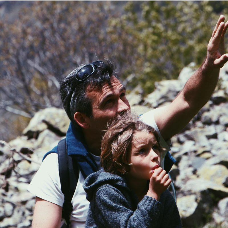 a man on a walk pointing upwards on a trail with a young boy with him