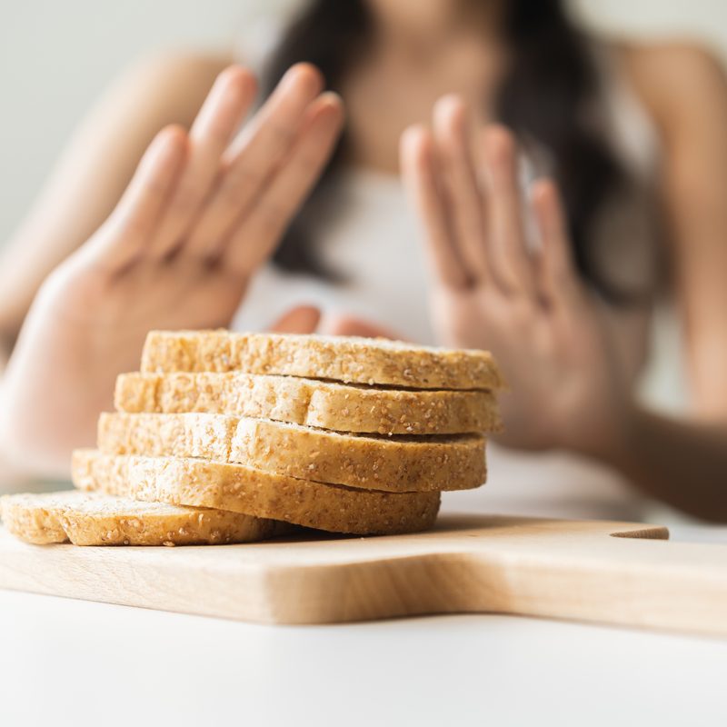Woman with hands pushed out, refusing to eat white bread slice on chopping board