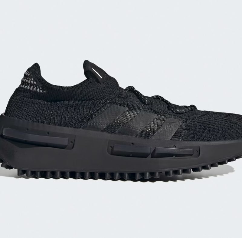 A side angle of the Adidas NMD_S1 shoes in black against a gray background.
