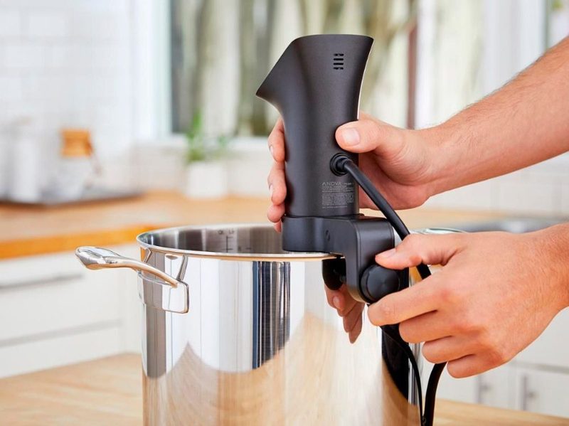 A man attaching an Anova Wifi Precision Cooker Pro to the side of a pot.