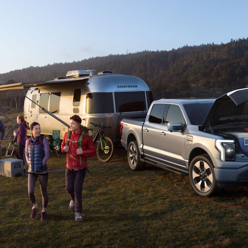 Ford F150 Lightning next to a camping trailer.