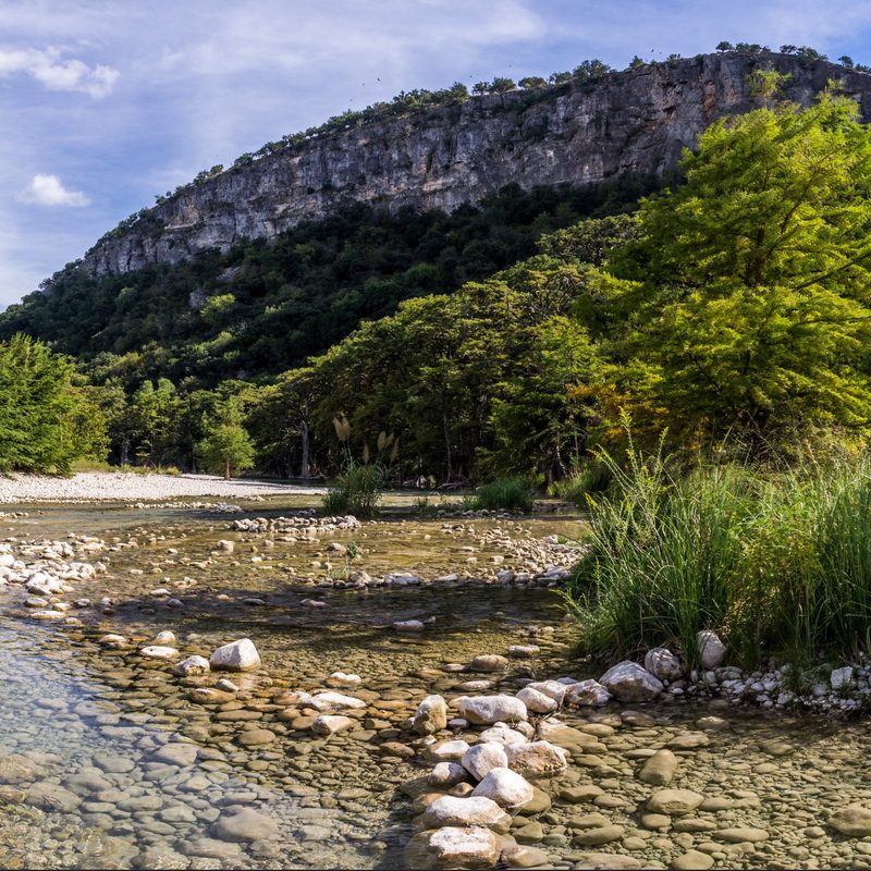 A shallow rocky bed of water with a view of Old Baldy mountain in Garner State Park
