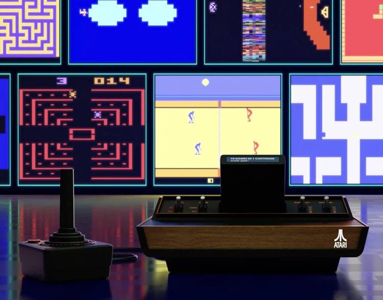 The Atari 2600+ system and joystick on a table with the games on a screen in the background.
