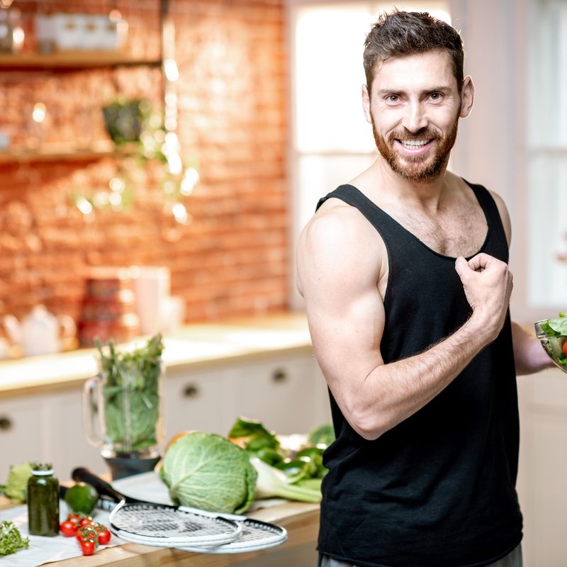 Man showing muscles, eating healthy vegetarian salad