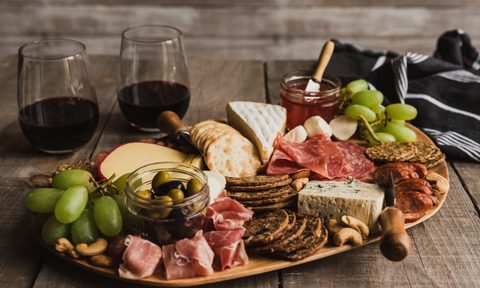 Close up of charcuterie board and glasses of wine on wooden table.