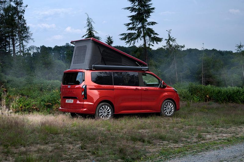 Ford Transit Nugget campervan parked in a field with its rooftop sleeper popped.