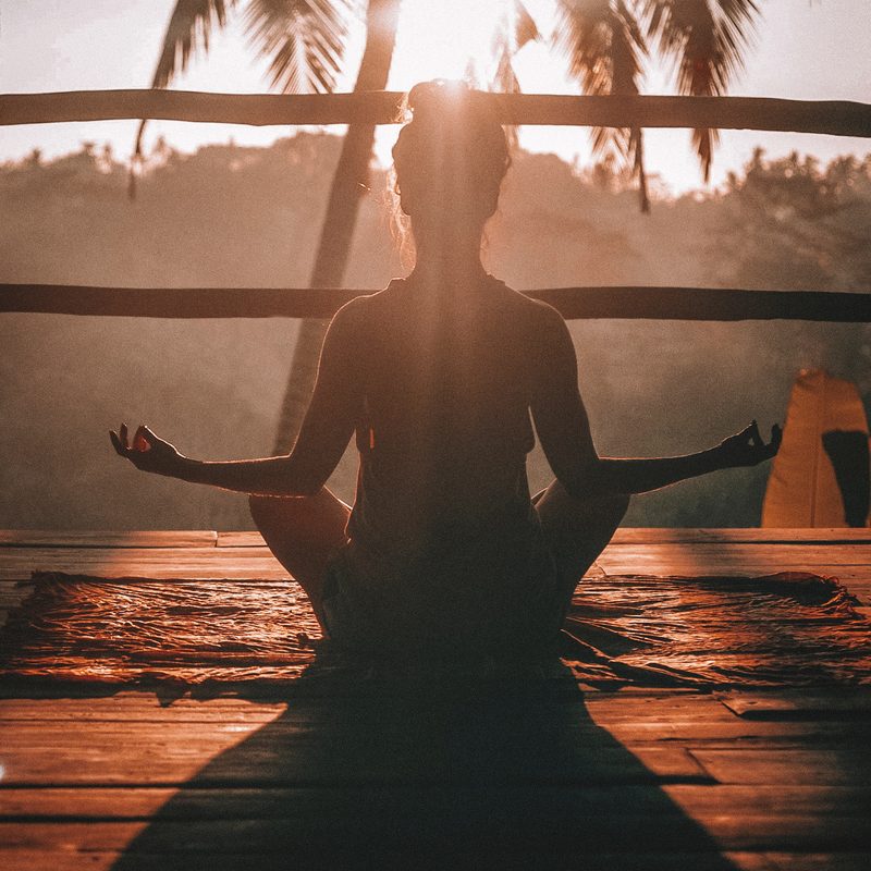 Silhouette of woman seated in yoga pose on deck sunset and palm tree