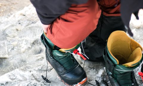 A man puts on a pair of snowboard boots in the parking lot.