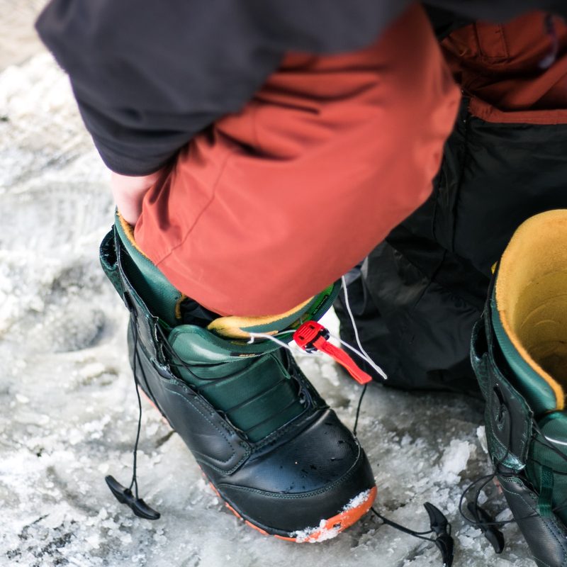A man puts on a pair of snowboard boots in the parking lot.
