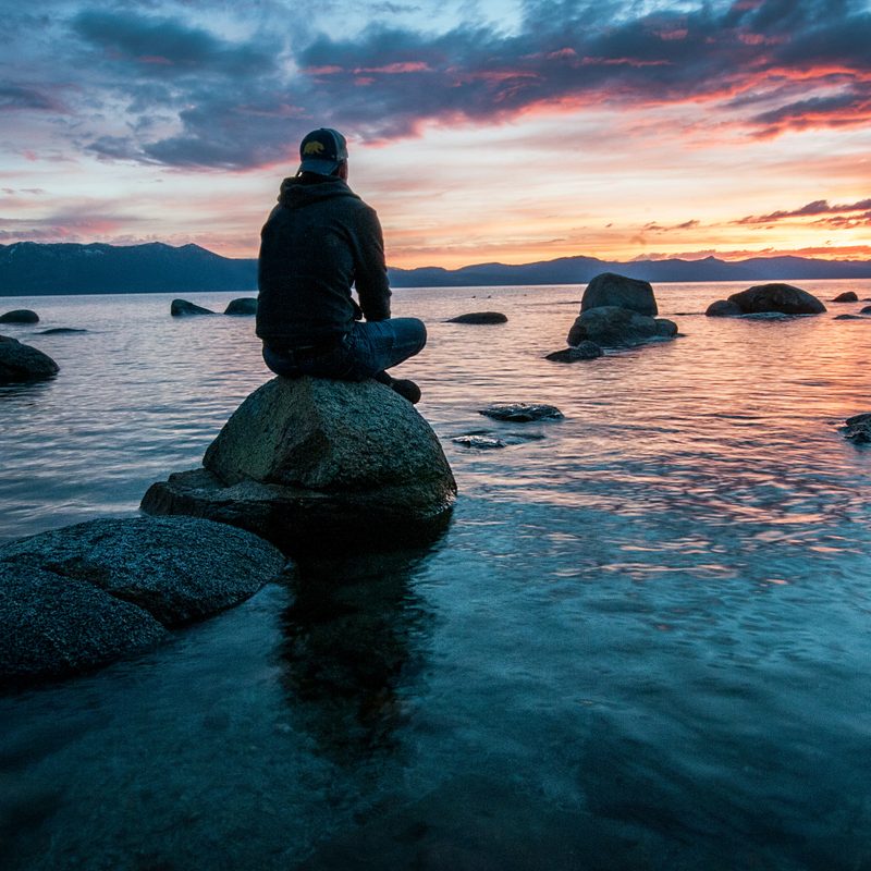 Silhouette man sitting meditating on rock by the ocean