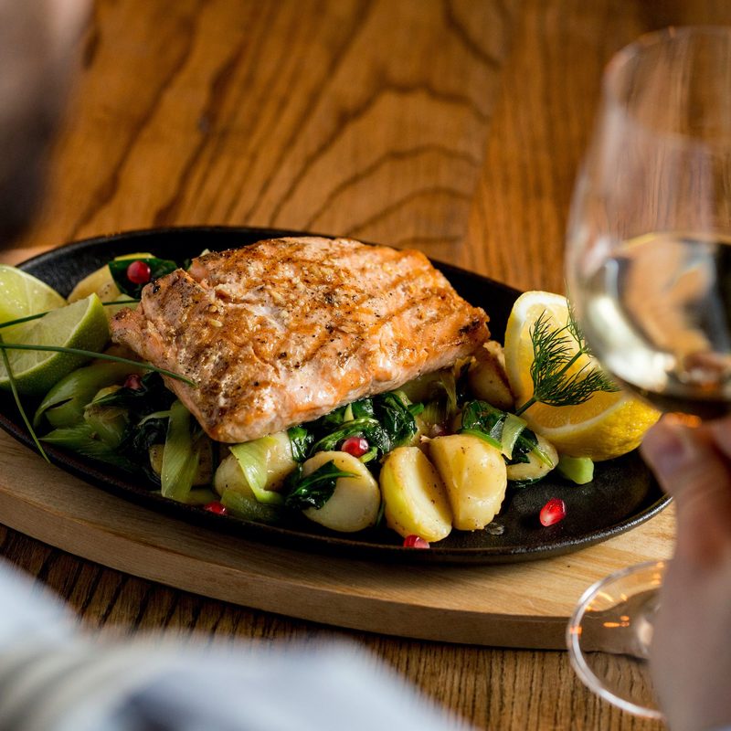 Young man eating salmon fillet with gratinated potatoes, leek and spinach in the restaurant with glass of white wine