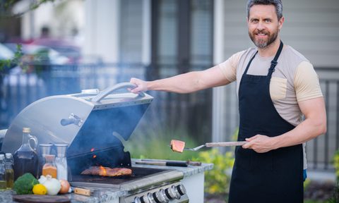 Male chef grilling and barbequing in garden. Barbecue outdoor garden party. Handsome man preparing barbecue meat. Concept of eating and cooking outdoor during summer time.