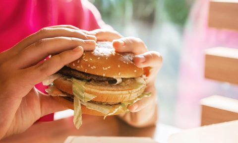 WARSAW, POLAND - SEPTEMBER 16, 2022: Woman with McDonald's burger at table in cafe, closeup