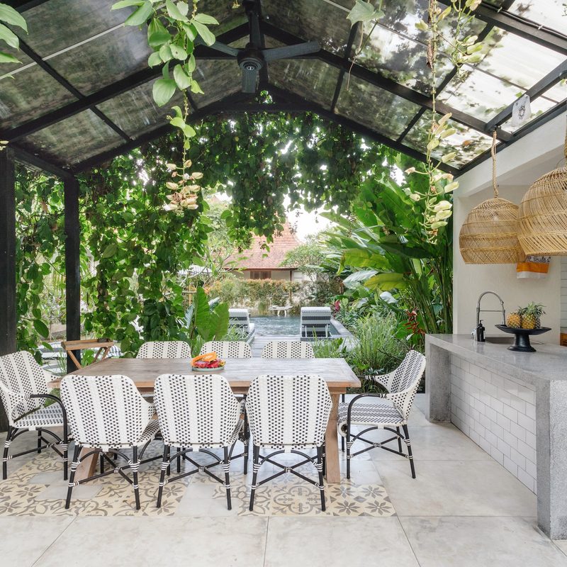 Open kitchen with empty dining room table and chairs outside, against green fresh plants on background