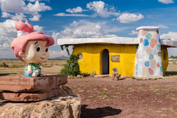 Statue of Pebbles sitting on a rock in front of a house.
