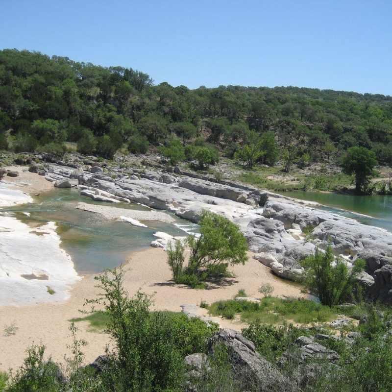 a unique limestone formation with pools of water along a line of trees in Pedernales State Park