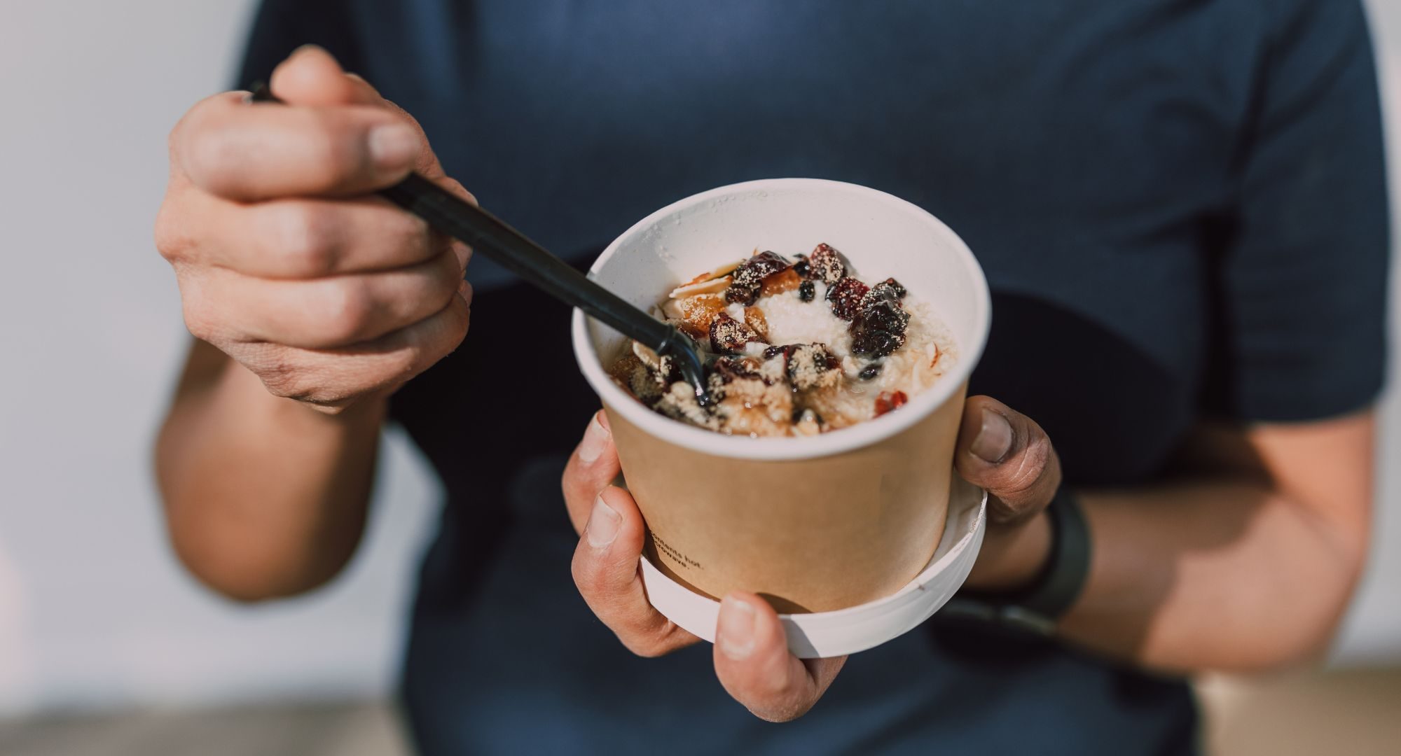 person in blue shirt holding a cardboard bowl of oatmeal