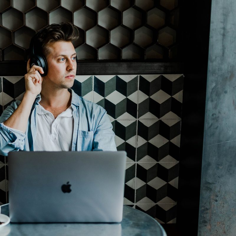 A person looking out the window while wearing headphones and working on a laptop