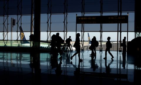 People walking through an airport with large windows in the background