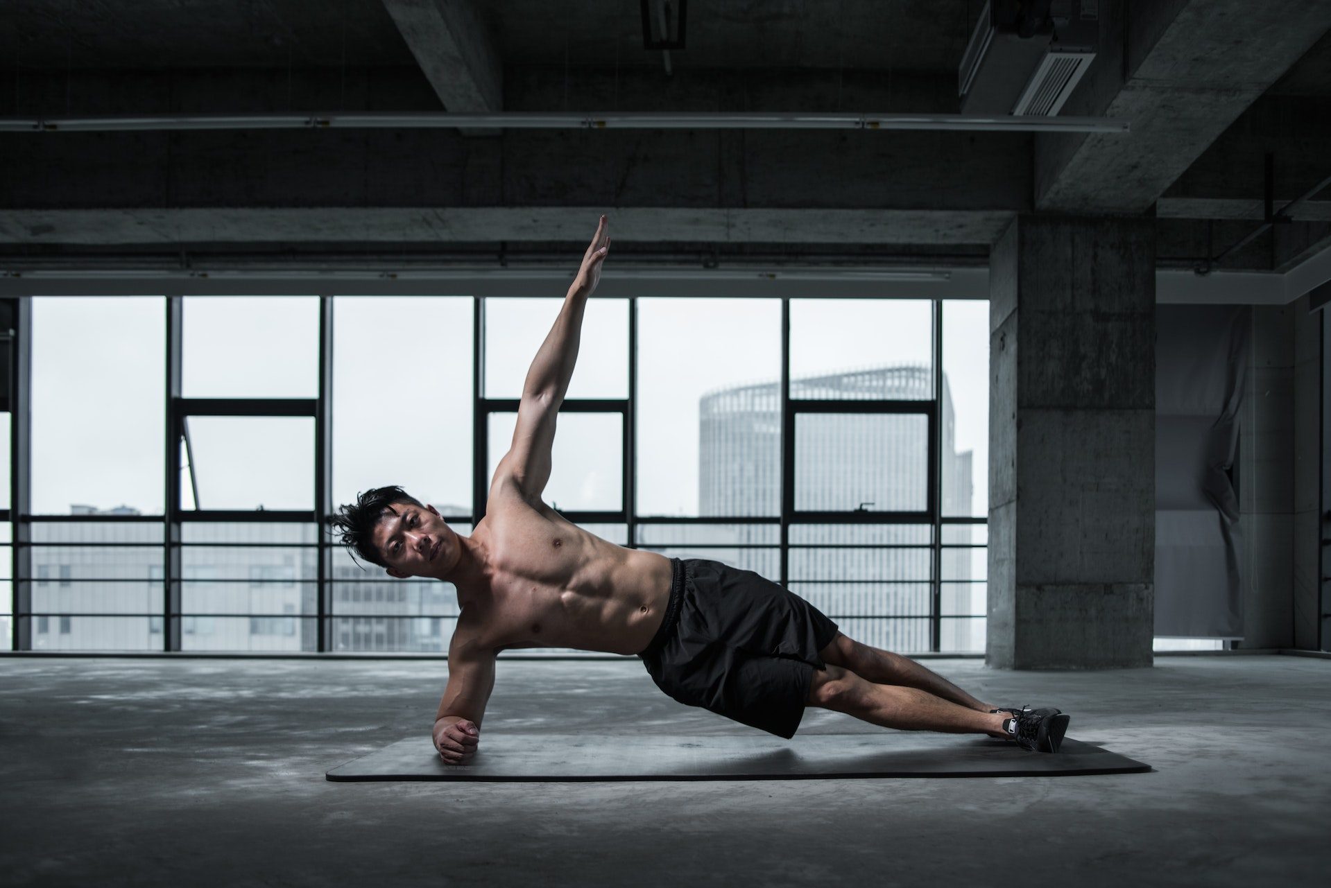 Man in side plank yoga pose on mat in studio in front of glass windows