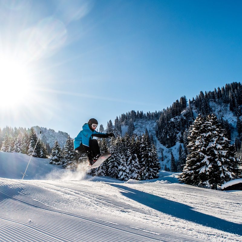 A snowboarder jumps off a ski jump onto the groomer.