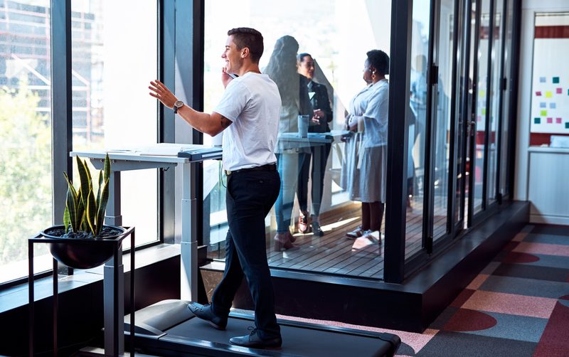 Shot of a young businessman talking on a cellphone and going through paperwork while walking on a treadmill in an office.