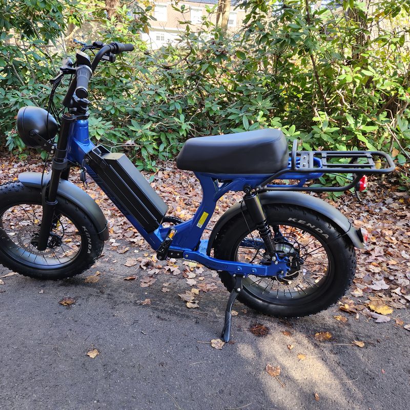 Juiced Bikes Scorpion X2 moped-style e-bike parked on asphalt with leaves and tress in the background