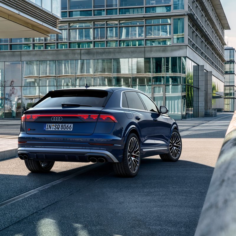 2024 Audi S Q8 in Waitomo Blue right rear three-quarter view in a city roadway between commercial buildings - European Model Shown.