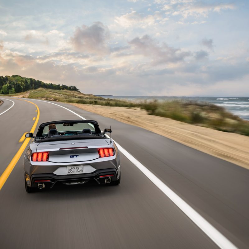 2024 Ford Mustang GT California Special convertible rear view as it drives down the road next to the beach on the right.