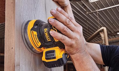 A man using a 20V DeWalt orbital sander on a piece of wood.