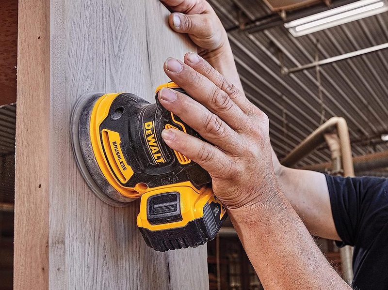 A man using a 20V DeWalt orbital sander on a piece of wood.