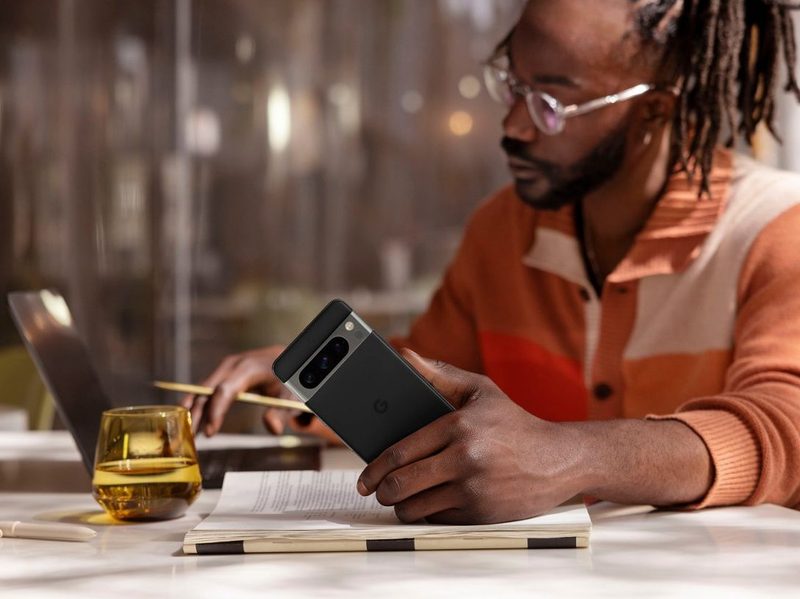 A man works on his laptop while holding a Google Pixel 8 Pro.